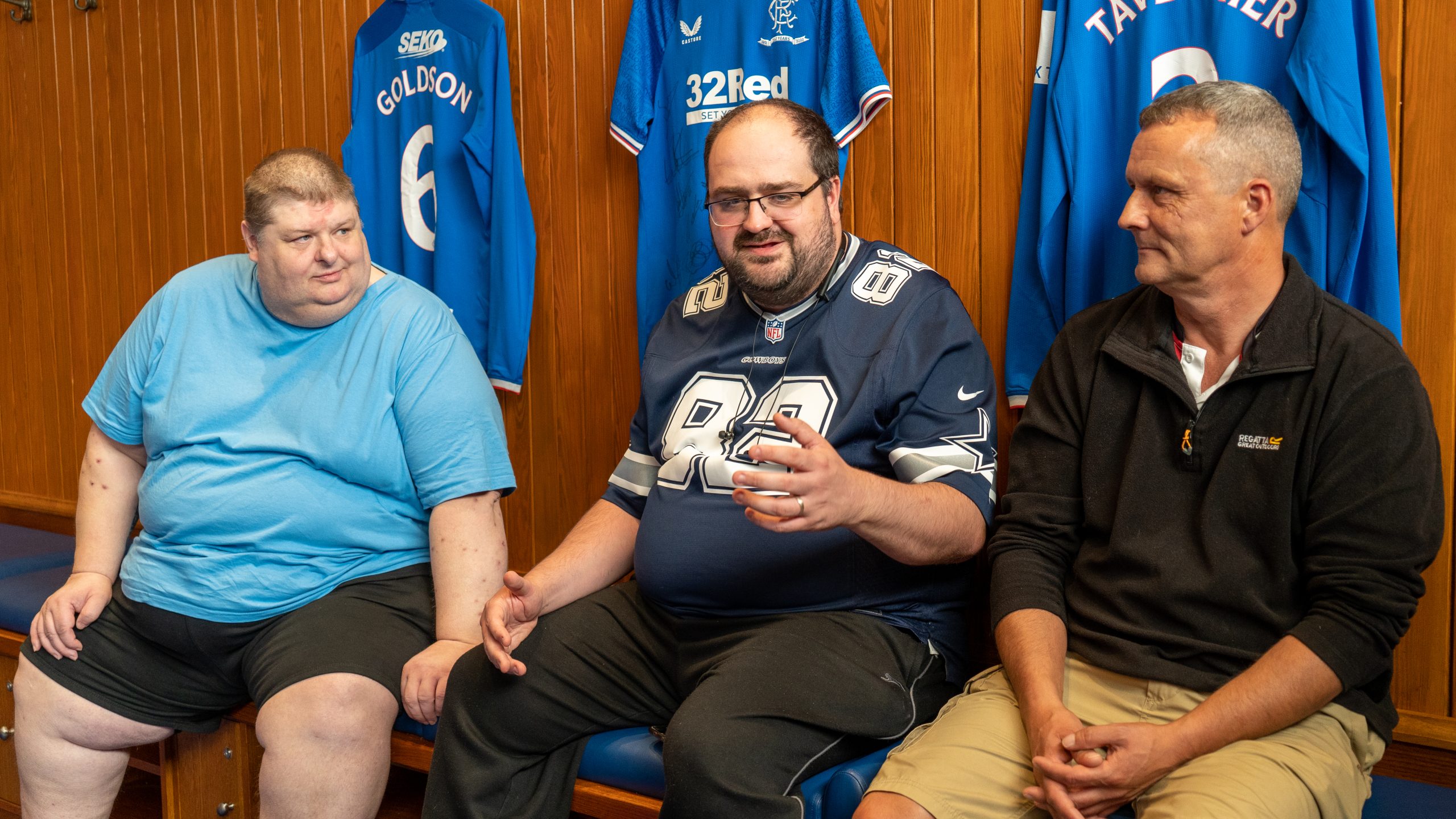 Three men sitting talking in football changing room