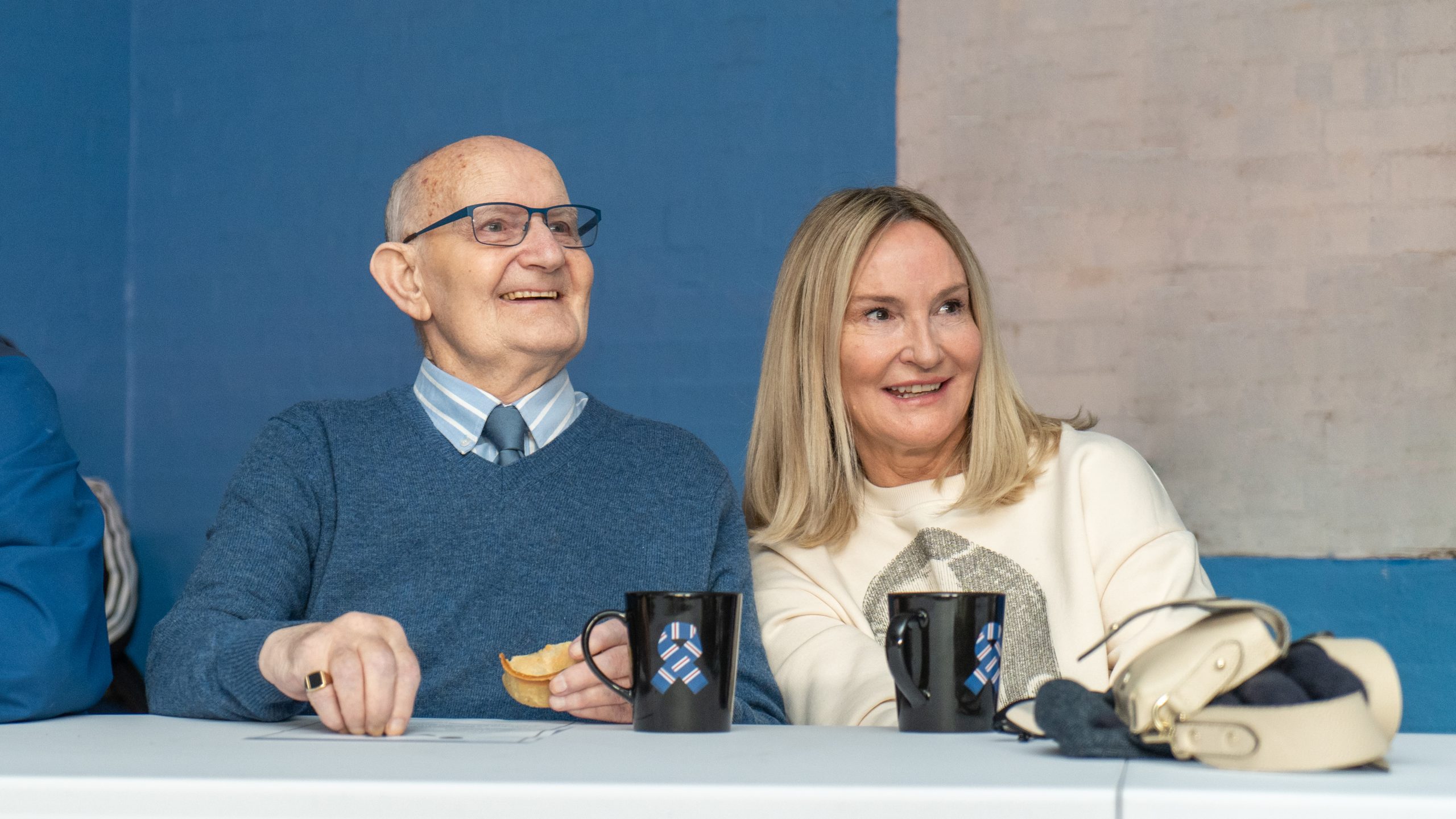 Older man and woman sitting with hot drinks