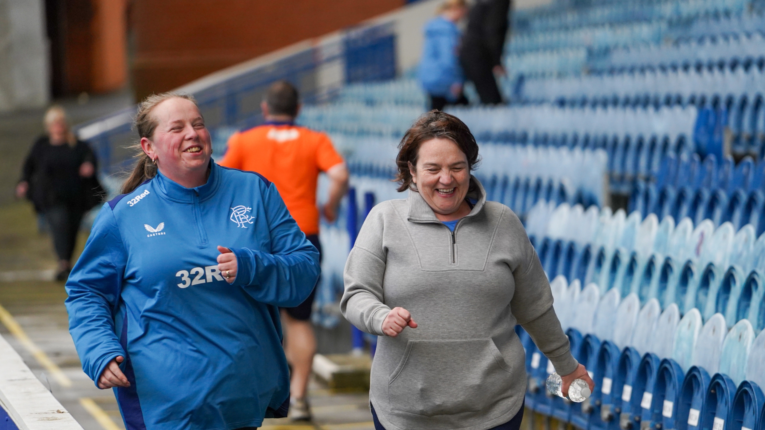 Two women smiling as they run around trackside at Ibrox Stadium