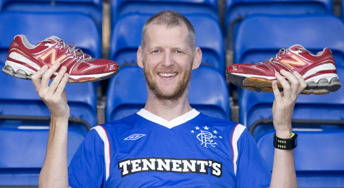 A man holding up two shoes in a Rangers top at Ibrox Stadium