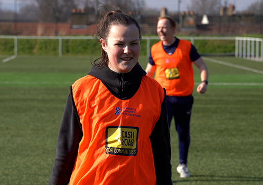 Female teenager smiling on football pitch wearing orange bib