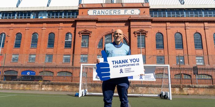 Alex Rae standing in front of Ibrox with a sign that says 