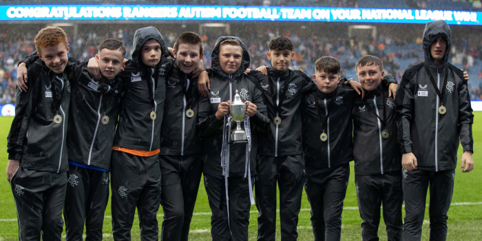 A group of young people standing pitch ide at Ibrox with a trophy