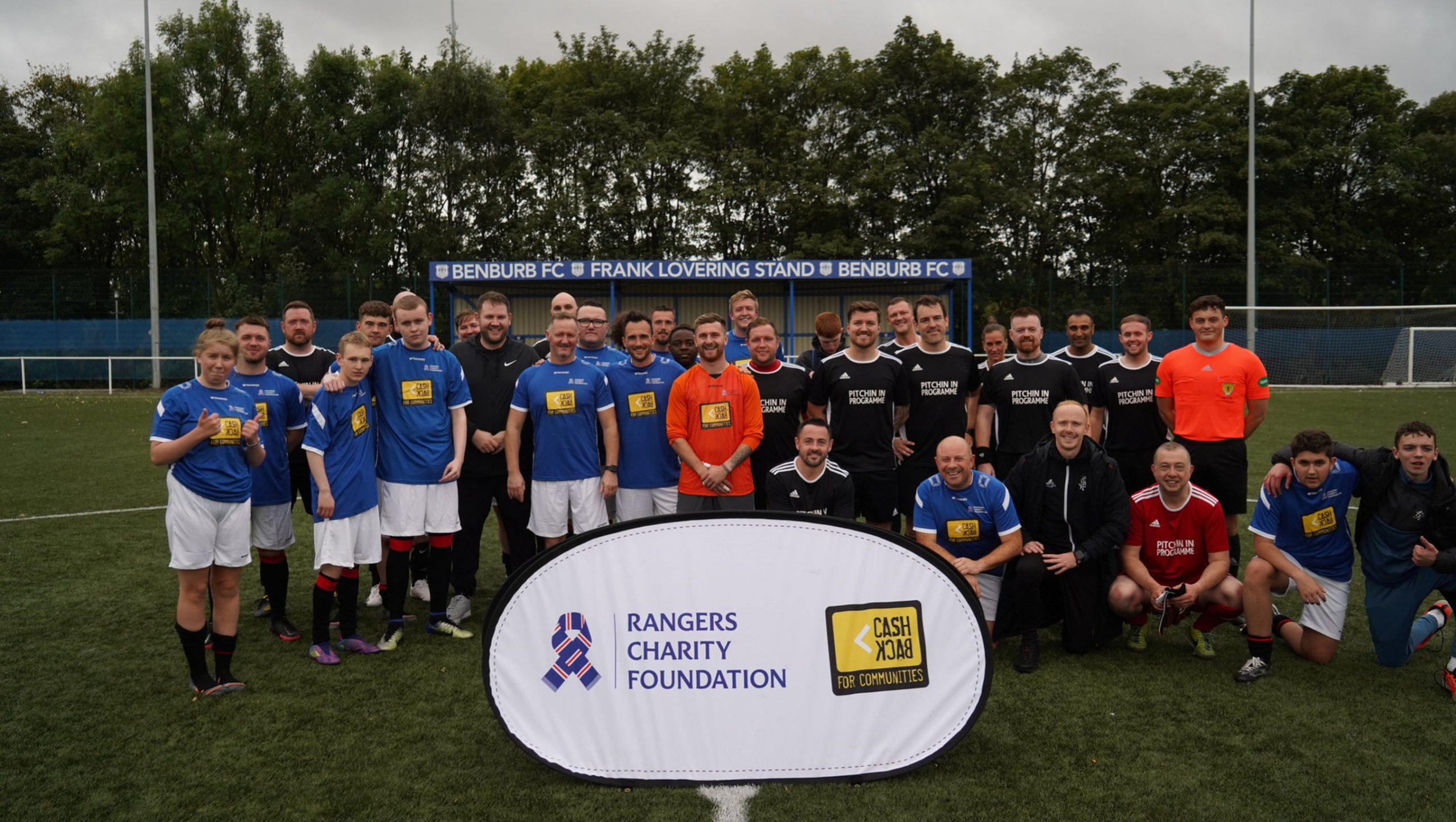 Group of people on football pitch with prop of Rangers charity Cash Back
