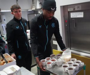 2 academy football players serve teas and coffees
