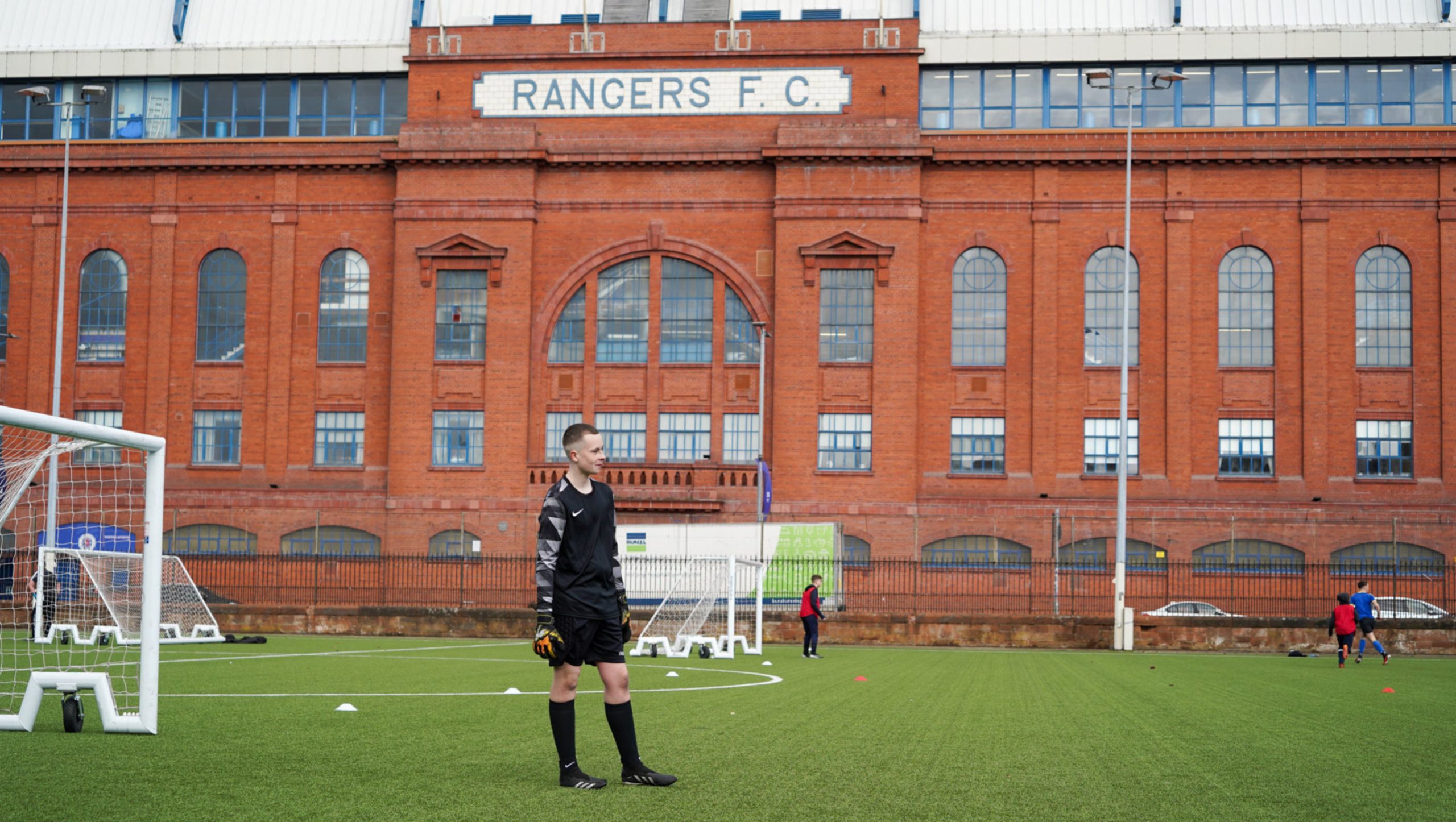 A young goalkeeper playing football next to Ibrox stadium