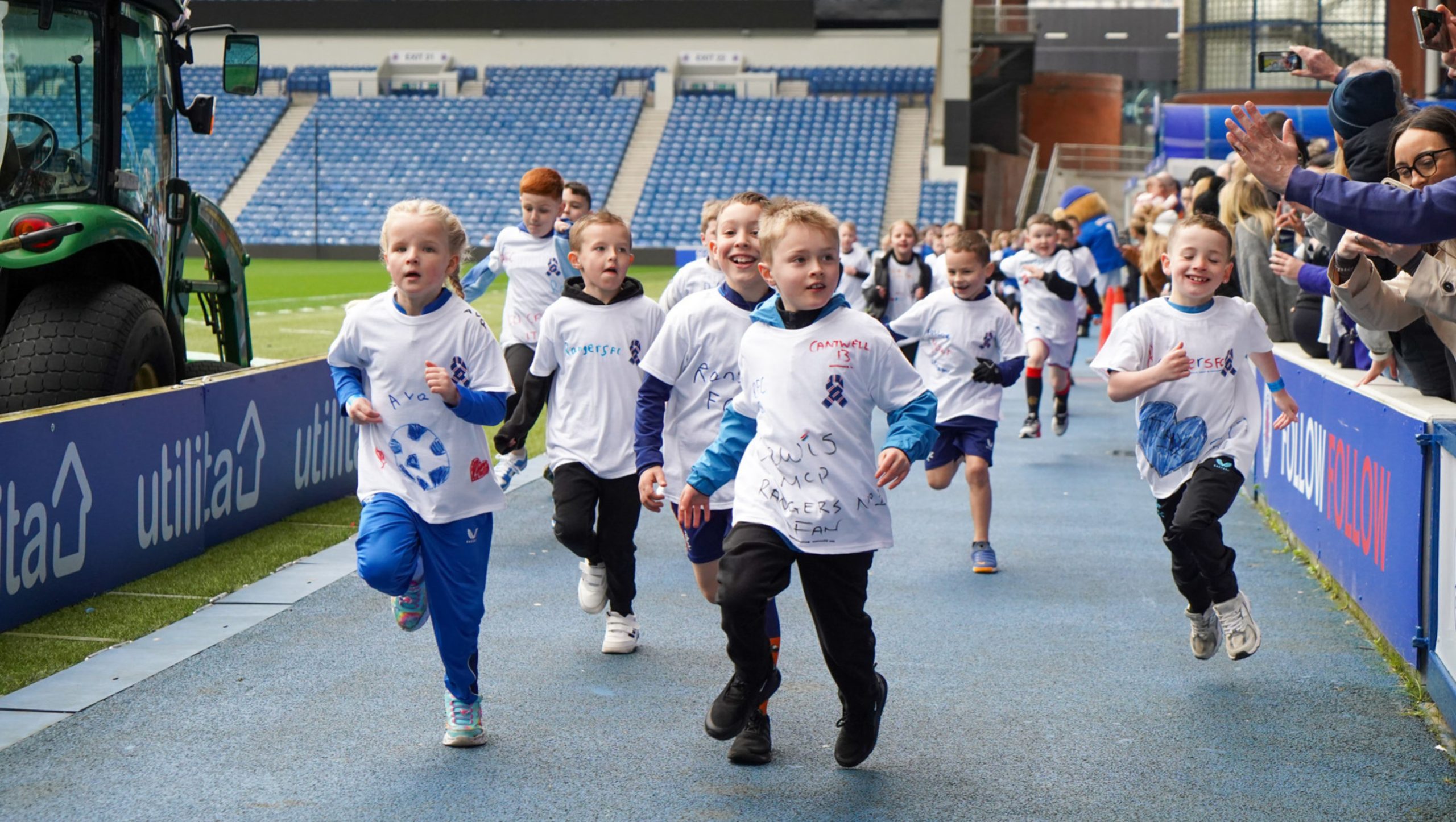 A group of children running round the pitch at Ibrox