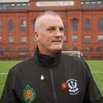 A veteran standing on a football pitch looking into the distance in front of Ibrox Stadium
