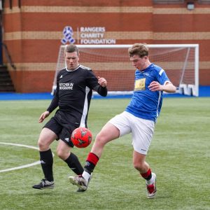 A CashBack participant and a Police Scotland Officer chasing a ball in a football match against each other.