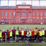 Four teams of school pupils posing for a group photo with Ibrox Stadium in the background.
