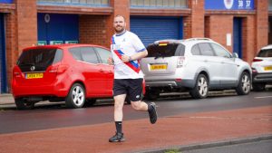 man in charity running top running outside ibrox Stadium