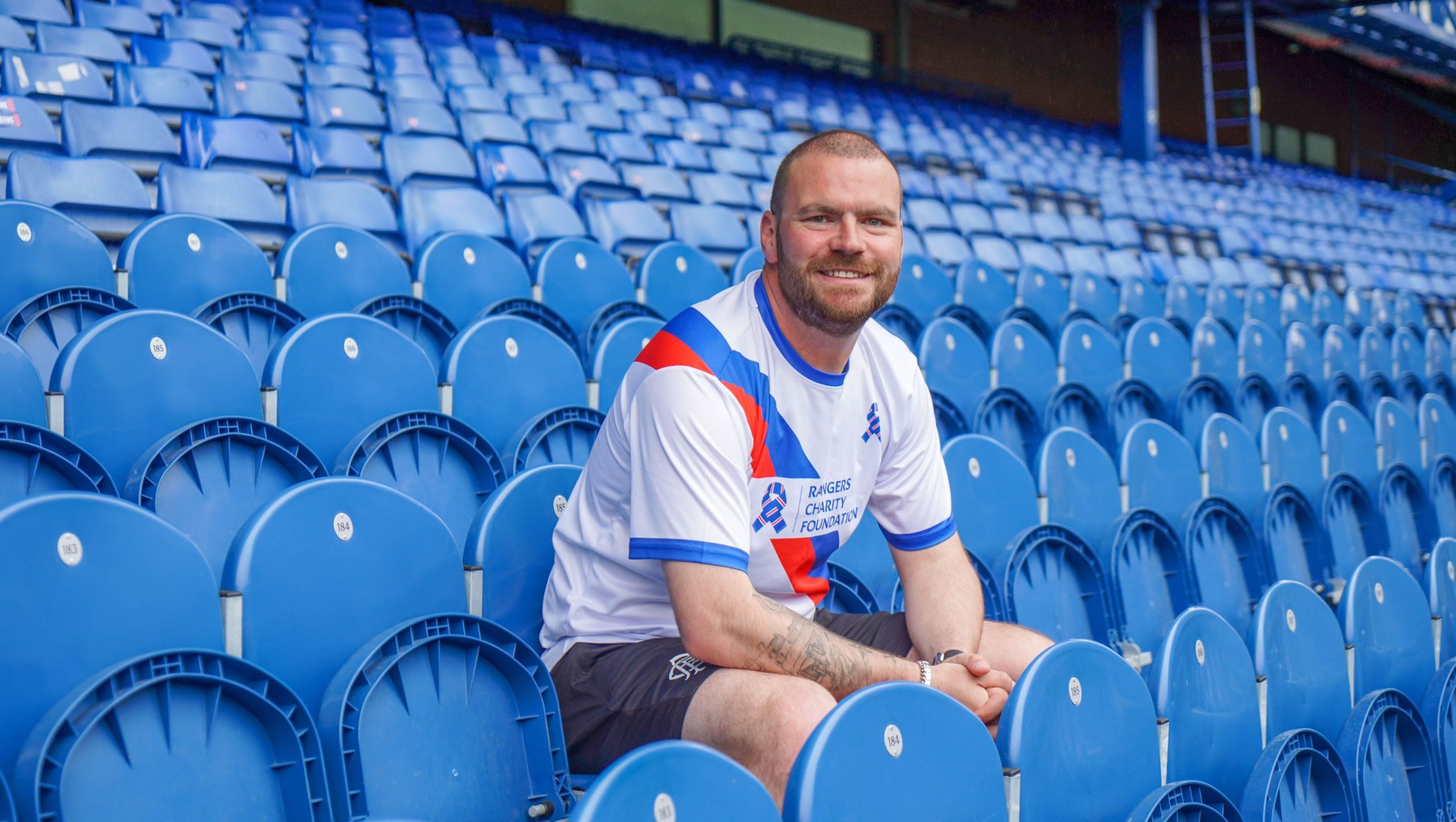 man in charity running top sitting in the stand at Ibrox stadium