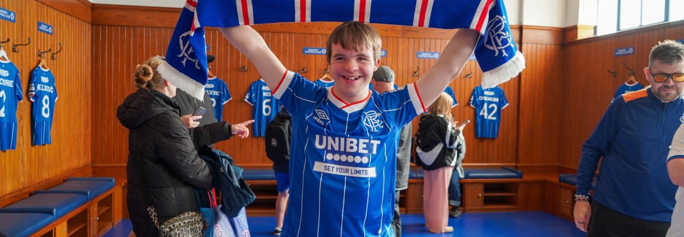 boy smiling in dressing room with rangers scarf